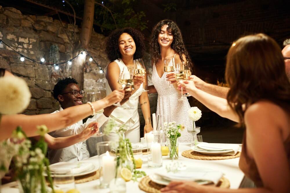 two-happy-young-intercultural-brides-toasting-with-their-wedding-guests-min